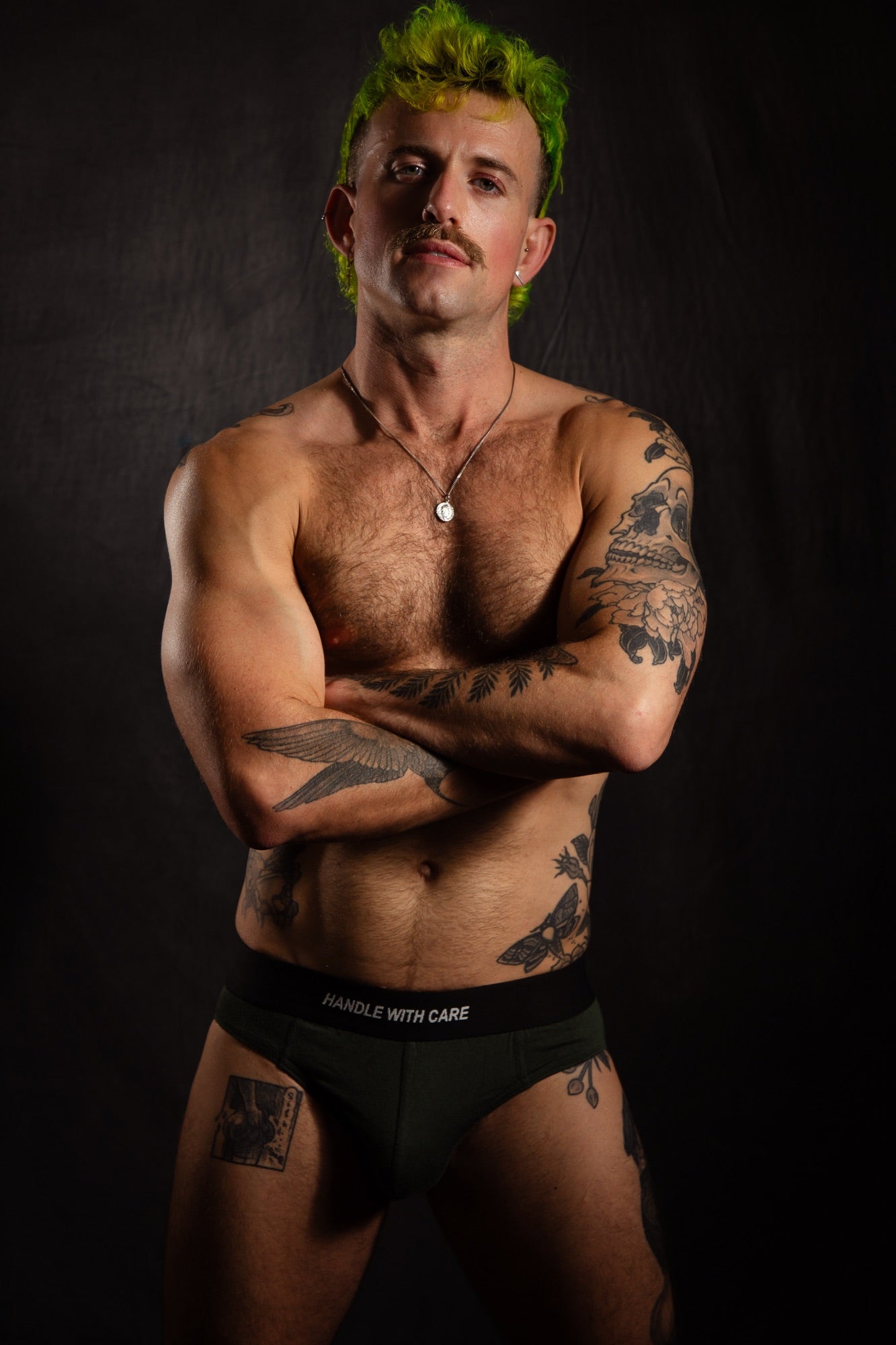 Man with tattoos wearing black underwear against a dark background