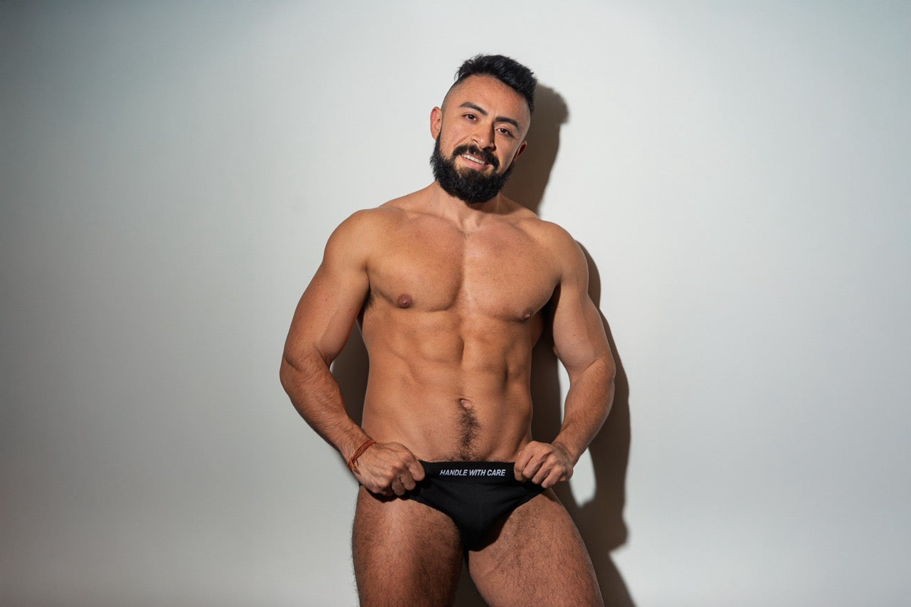 Man wearing new Unapologaytic black briefs with a visible waistband slogan reading Handle with Care against a plain background