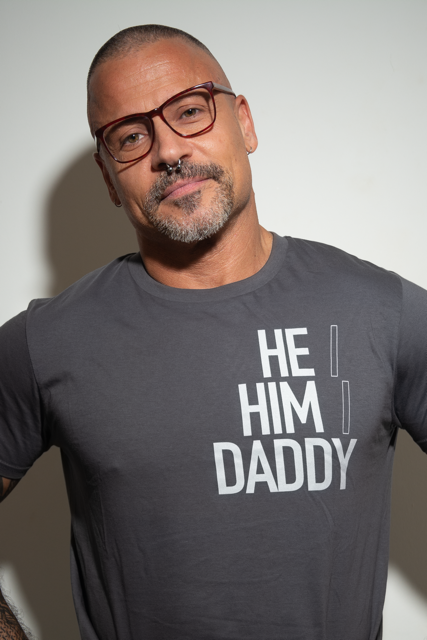 A handsome man wearing a grey organic cotton t-shirt with the text 'HE HIM DADDY' on the front.